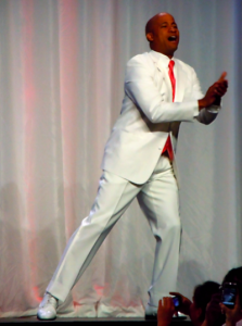 excited groom in a white suit, white shoes, and bright pink tie