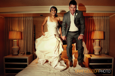 Bride in ivory gown and groom in gray suit with brown shoes jump on a bed
