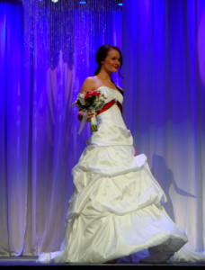 bride in white gown with red sash at fashion show